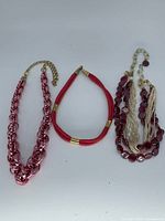 All three necklaces laid out: pink chain, red braided, multi-strand burgundy