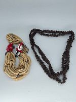 Both necklaces laid flat: tan multi-strand with bird beads, brown seed bead necklace