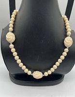 Necklace front on display bust showing carved focal beads and spacer arrangement