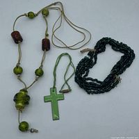 All three necklaces laid out: cube-bead strand, cross pendant, cord necklace with beads