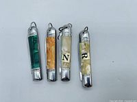 Front view of four closed miniature pocket knives showing handle colors and keychain loops