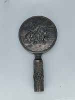 Front view of closed mirror showing repoussé scene and handle detail