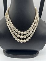 Front view showing three graduated strands of cream faux pearls on display bust