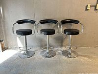 Front view of three matching black leather bar stools on chrome bases