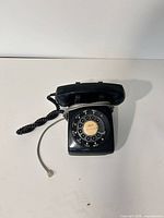 Front angled view of entire black rotary dial telephone with cords
