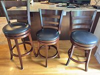 Front view of three dark brown wood swivel bar stools showing ladder backs and round black seats