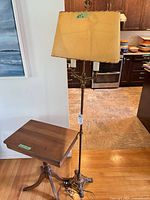 Full view of brass floor lamp with shade alongside wooden tilt-top table