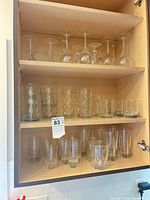 Cabinet with three shelves of assorted clear glass stemware, highball, rocks and tumblers
