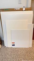Front view of stacked white foamcore and matboard sheets showing size variation