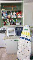 Overview showing ironing board, stool, basket, cabinet of cleaning products
