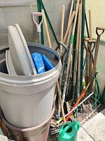 Overall lot with trash bin, tarps, watering can, various long-handled tools and plant supports