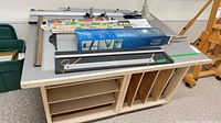 Mat cutter, rails, rulers, cutting heads and supplies on laminate-topped cabinet