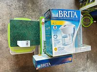 Brita pitcher box, FoodSaver boxes, decorative tin and green-lidded container visible