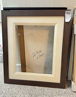 Front view of framed piece showing dark brown frame with cream mat and glass