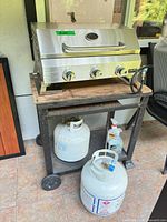 Full view of grill on cart with two propane tanks and cleaner bottle