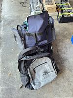 Roots backpack, navy duffel, black suitcase and reusable bags visible