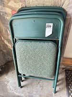 Four folded green metal chairs showing padded seat pattern