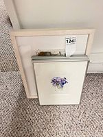 Two frames stacked, showing silver metal-framed purple floral watercolour and light wood-framed abstract landscape