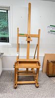 Front view of solid wood H-frame studio easel showing mast, tray, casters