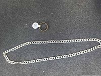 Ring and curb chain necklace laid out on dark surface