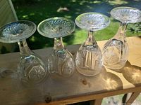 Four upside-down clear crystal cordial glasses showing starburst-cut bases and pressed patterns