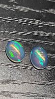 Two oval cabochon opals on black surface showing green and red flashes