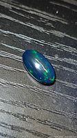 Oblique view of oval black opal cabochon showing green and red play-of-color