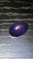 Oval cabochon black opal showing dark body tone with red pinfire