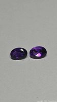 Two oval-cut deep purple gemstones on neutral background