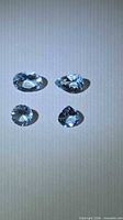 Four pale blue faceted aquamarines arranged in two rows on neutral background