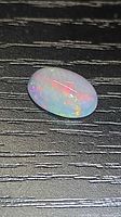 Oval opal cabochon on black textured background showing play of color