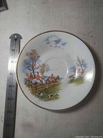 Front view of saucer showing fox-hunt print and gold rim beside ruler