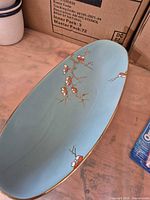 Top view of turquoise oval platter with floral branch design and gold rim