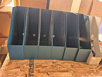 Front view of six teal and one beige magazine file holders lined side by side