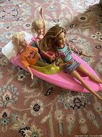Three dolls seated in pink boat on rug