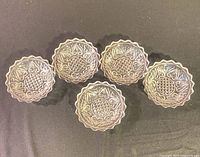 Five clear pressed glass ashtrays displayed face up