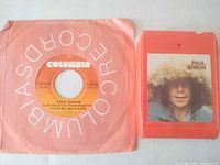 Front view of 7" single in sleeve beside front of 8-track cartridge