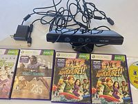 Front view of Kinect sensor, power supply, USB adapter, four game cases and loose disc