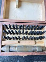 Open wood box showing three rows of steel stamps, knurled handle stored in lower compartment