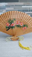 Pierced bamboo fan with painted flowers and tassel on stand