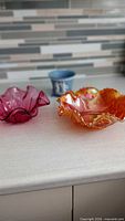Overview of cranberry dish, carnival glass bowl, and jasperware planter on countertop