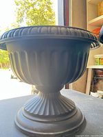 Side view of one black pedestal planter showing fluted bowl and ribbed base