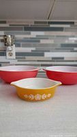 Front view showing yellow handled casserole bowl with floral motif and two pink mixing bowls behind