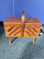 Closed wooden cantilever sewing box on legs, handle upright