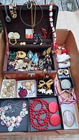 Overview of entire lot inside cardboard box, jewelry arranged around small wooden box