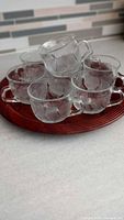 Seven clear glass mugs stacked on a wooden tray