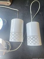 Two white cylindrical pendant lights showing shade design and stems