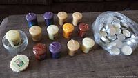 Group view of 13 votives, wax melt tart, glass bowl melter and bag of tea lights on table