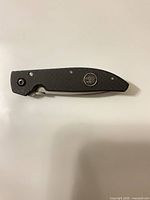 Knife closed, showing black G-10 handle, medallion, lanyard hole