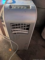 Full view of portable air conditioner showing cabinet, power cord and damaged grille